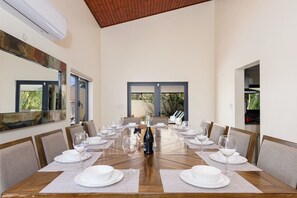 A dining room with a long table set for a meal, large windows, and a ceiling fan. - Luxury 6BR Villa w/ Private Pool near Palm Beach (Noord)