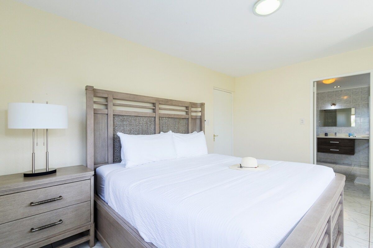 Ein Hotelzimmer mit Bett, Nachttisch, Lampe und einem Badezimmer mit Spiegel und Waschbecken.