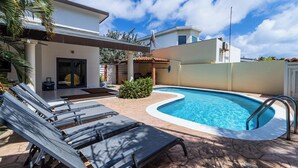 A swimming pool with lounge chairs, a covered patio, and a clear blue sky. - Luxury 6BR Villa w/ Private Pool near Palm Beach (Noord)
