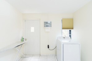Une buanderie équipée d’un lave-linge, d’une planche à repasser et d’une porte.