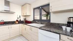 A modern kitchen with light wood cabinets, a granite countertop, a stainless steel range hood, and a window with a view. - Luxury 6BR Villa w/ Private Pool near Palm Beach (Noord)