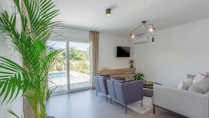 Ein modernes Wohnzimmer mit einer Couch, Sesseln, einem Fernseher und einer großen Pflanze.