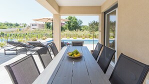 Eine überdachte Terrasse mit Tisch, Stühlen und einer Obstschale.