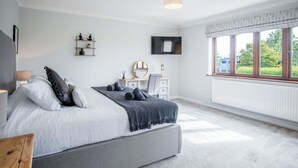 A bedroom with a bed, bedside table, dresser, and a window with a view of greenery. - Springfield Lodge - 3 Bedroom Home - Princes Gate (Narberth)