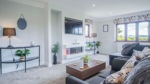 A modern living room with a fireplace, black sofas, a coffee table, and potted plants. - Springfield Lodge - 3 Bedroom Home - Princes Gate (Narberth)