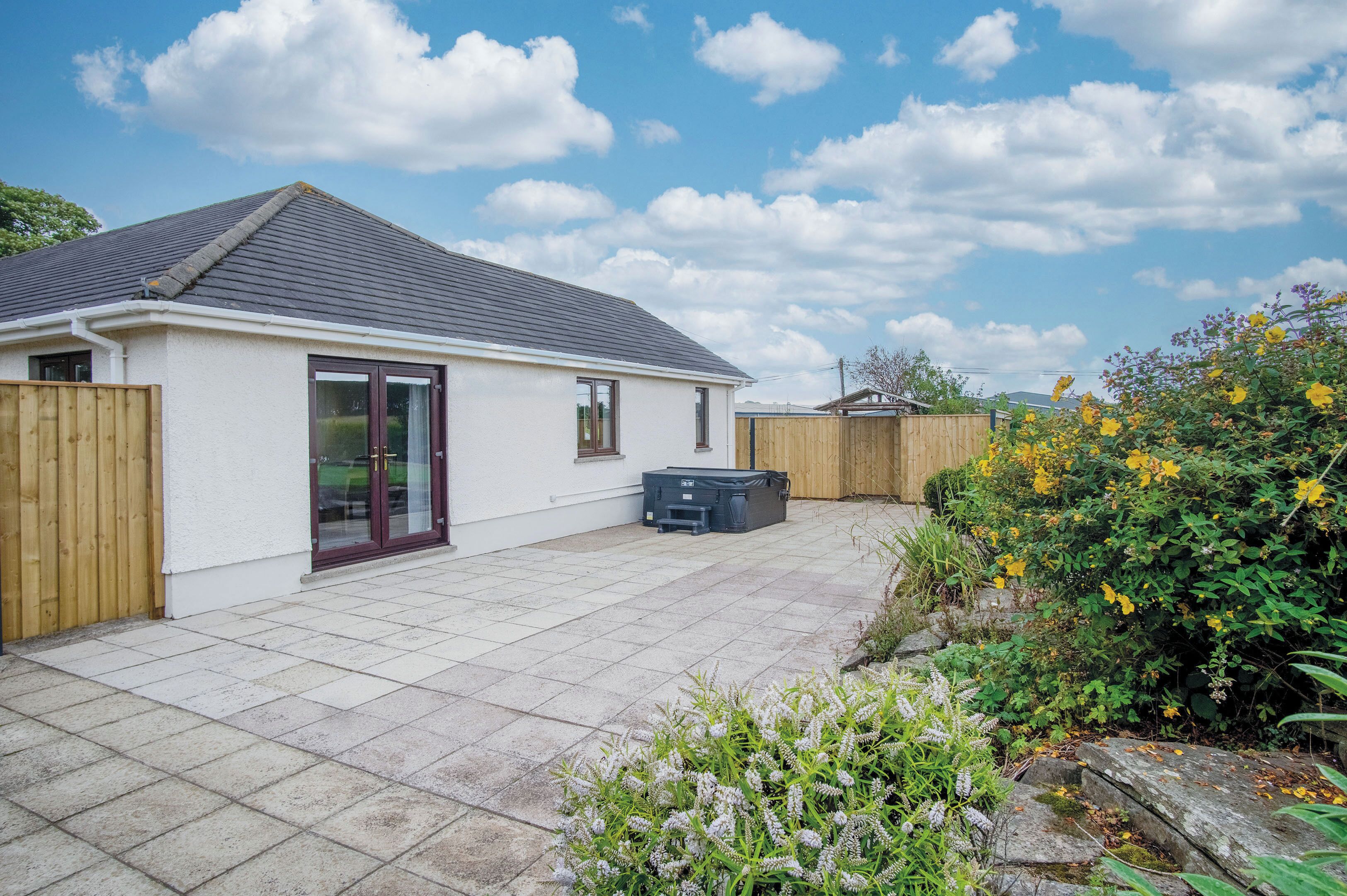 A house with a tiled patio, a wooden fence, and a garden with yellow flowers.