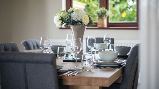 A dining table set with plates, bowls, and wine glasses, with a vase of flowers in the center. - Springfield Lodge - 3 Bedroom Home - Princes Gate (Narberth)