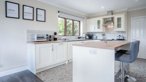 A modern kitchen with white cabinets, a central island, and a bar stool. - Springfield Lodge - 3 Bedroom Home - Princes Gate (Narberth)