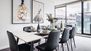 Un espace repas avec une table blanche, des chaises noires et une vue sur la ville grâce à de grandes fenêtres.