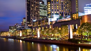 Un hôtel situé au bord de l’eau, doté d’une architecture moderne, avec une rivière en premier plan et des fenêtres illuminées.