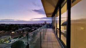 Un balcon avec vue sur la ville, des garde-corps en verre et un sol carrelé.