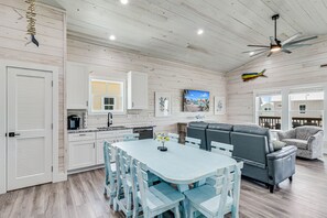 A spacious kitchen with white cabinetry, a dining area with blue chairs, and a gray sofa.