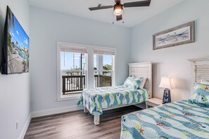 A bedroom with two beds, a ceiling fan, and a large window with a view of the outdoors.
