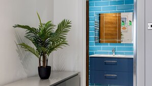 Ein modernes Badezimmer mit blauen Fliesen an der Wand, einem spiegeln Rahmen aus Holz und einer Topfpflanze auf einer weißen Arbeitsplatte.