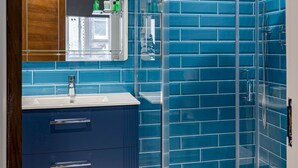 Ein Badezimmer mit blauen Fliesenwänden, einer Duschkabine aus Glas, einem weißen Waschbecken und einem Holzschrank.