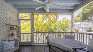 Une véranda couverte avec un ventilateur de plafond, un lit, une table et une chaise.