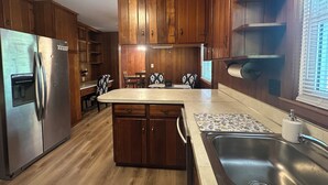 Une cuisine avec des meubles en bois, un réfrigérateur en acier inoxydable, une table à manger avec des chaises et un évier encastré.