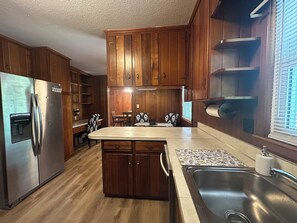 A kitchen with wooden cabinets, a stainless steel refrigerator, a dining table with chairs, and a built-in sink.