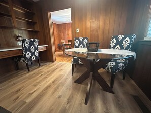 Puupaneloitu huone, jossa on pyöreä lasipöytä ja kuviollisia tuoleja.