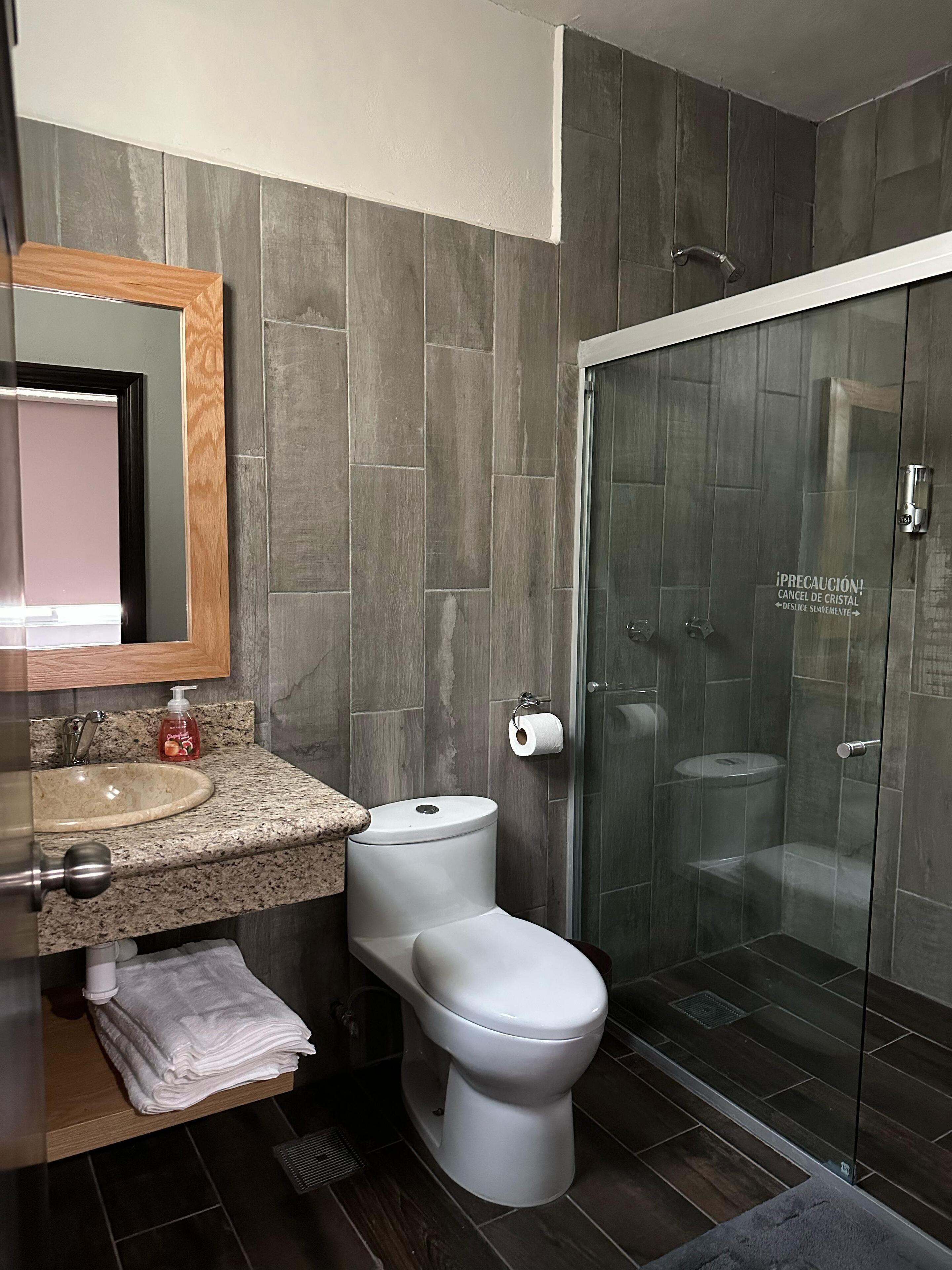 Un baño moderno con lavamanos de granito, inodoro blanco y ducha con cerramiento de vidrio.