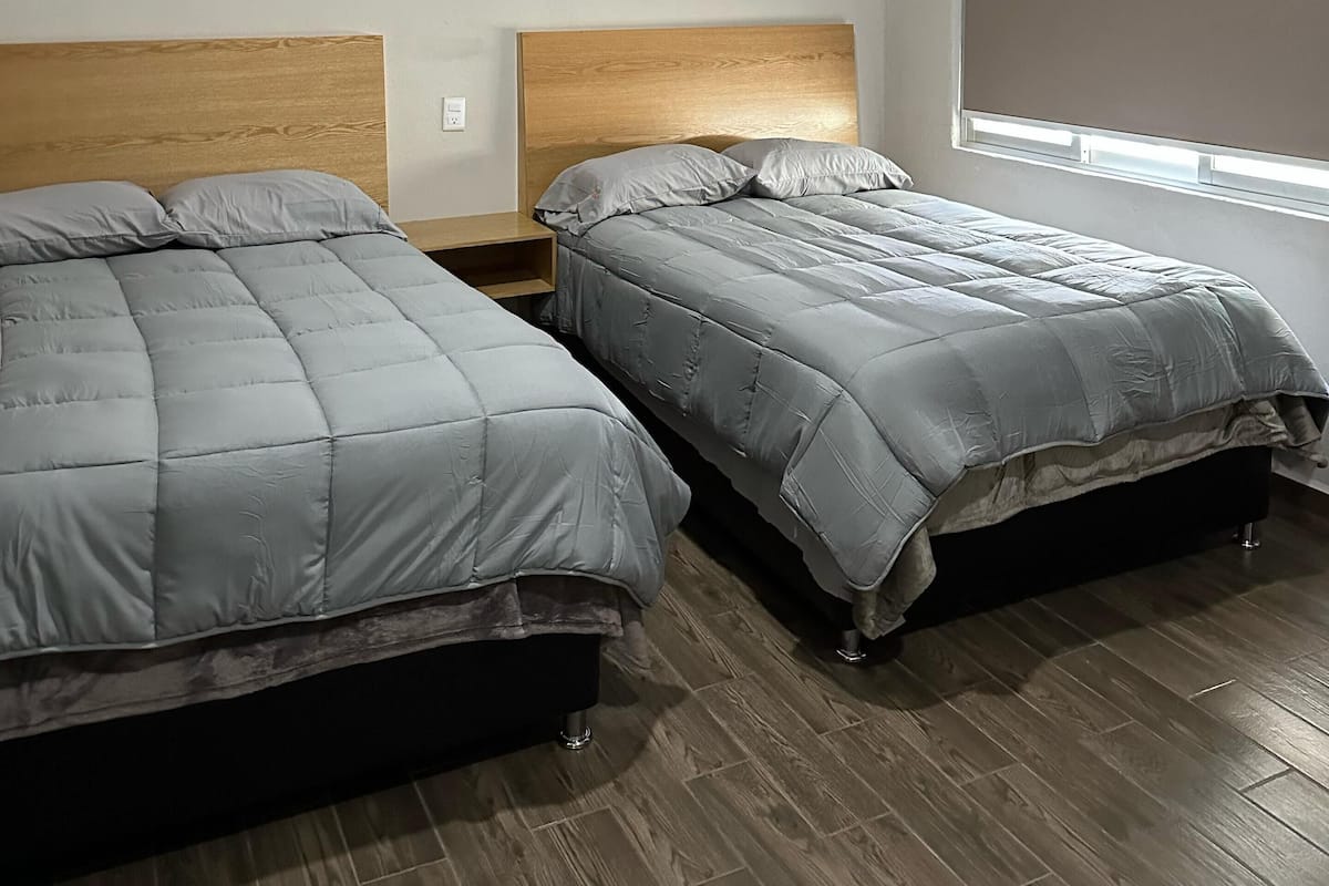 A room with two beds, wooden headboards, a window with blinds, and a ceiling light.