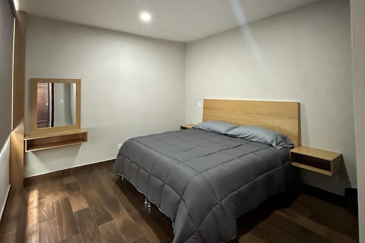 A bedroom with a bed, wooden headboard, bedside tables, a mirror, and a window.