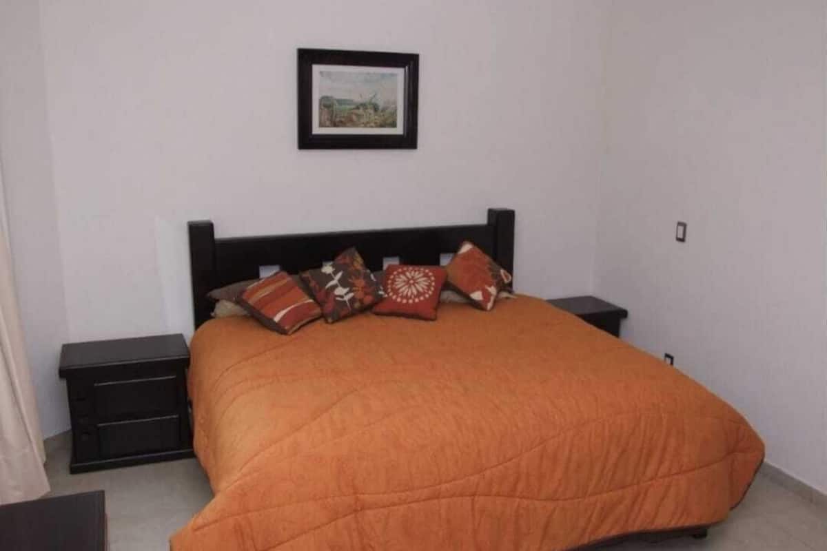 A bedroom with a bed, a nightstand, a framed picture on the wall, and a small table.
