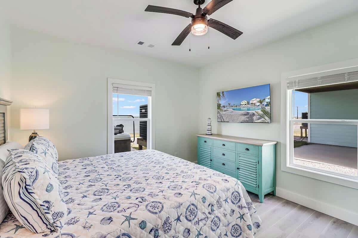 Un dormitorio con una cama, ventilador de techo, ventana, cómoda y un cuadro.