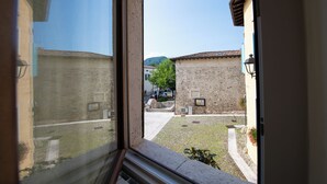 Blick durch ein Fenster auf einen Innenhof mit Steinhäusern, einem klaren Himmel und einem entfernten Berg.