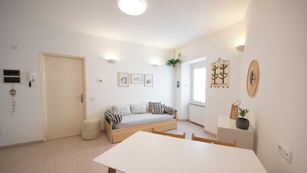Ein heller, minimalistischer Wohnraum mit Sofa, Esstisch und kleiner Küchenzeile.