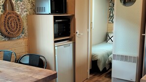 A compact kitchen with a refrigerator, microwave, and a small oven. There is a dining table with chairs and a wooden ceiling. - Cottage Cosy Aux Lauriers à Lacroix sur Meuse (Lacroix-sur-Meuse)