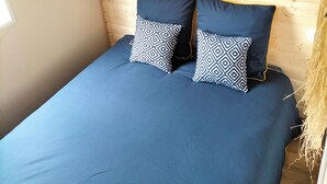 A bed with a blue mattress and patterned pillows, a wooden headboard, and a wall with a tropical leaf pattern. - Cottage Cosy Aux Lauriers à Lacroix sur Meuse (Lacroix-sur-Meuse)