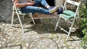 Un homme est assis sur un banc devant un bâtiment en pierre, et le chiffre « 12 » est inscrit au-dessus de l’entrée.