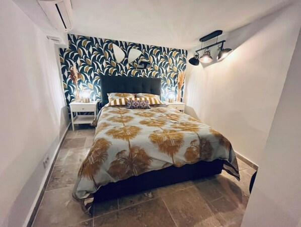 A bedroom with a bed, a nightstand, a wall with a leaf pattern, and a ceiling light fixture. - Triplex de Saint-paul Free Public Parking (Saint-Paul-de-Vence)