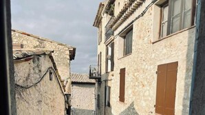 Une ruelle étroite pavée, bordée de bâtiments en pierre dotés de portes en arc de cercle et de volets en bois.