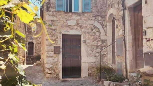 Un bâtiment en pierre avec une porte centrale et des fenêtres en arc de cercle, entouré d’une cour pavée.