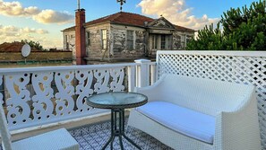 A balcony with a white wicker sofa and a small round table, overlooking a historic building with a red roof. - hi Hotel Ivy Buyukada (Adalar)