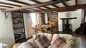 A cozy living room with a sofa, wooden dining table, and bookshelves. - Coastal South Devon cottage near Thurlestone and Salcombe (Kingsbridge)