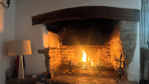 A stone fireplace with a fire burning inside, a lamp, and a kettle on the mantel. - Coastal South Devon cottage near Thurlestone and Salcombe (Kingsbridge)