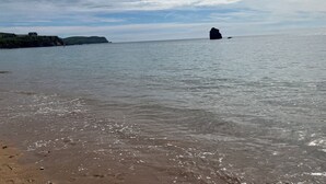 A beach with calm waters, a distant rock formation, and a grassy cliff with buildings. - Coastal South Devon cottage near Thurlestone and Salcombe (Kingsbridge)