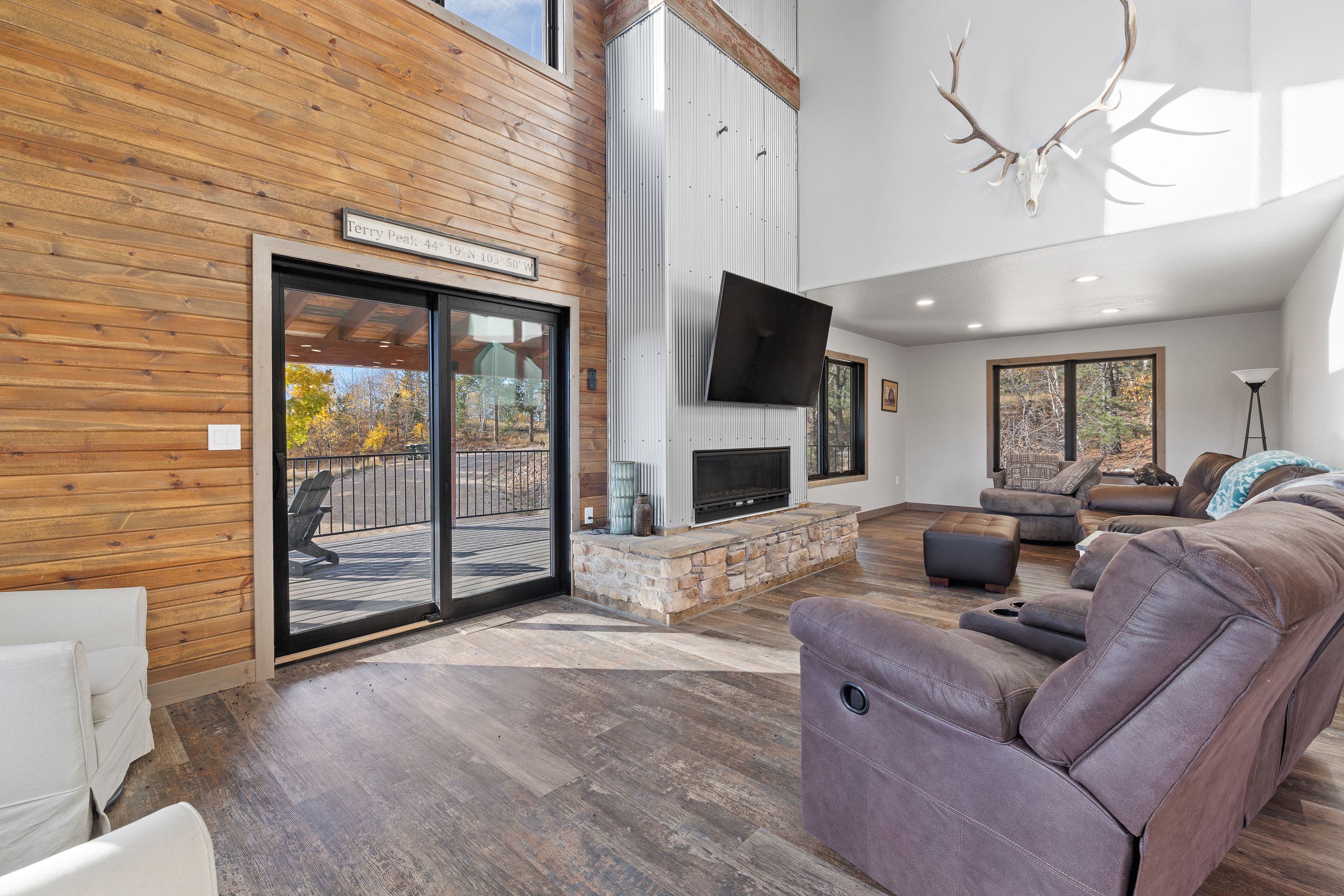 A modern living room with a stone fireplace, leather seating, and a large TV mounted on the wall.
