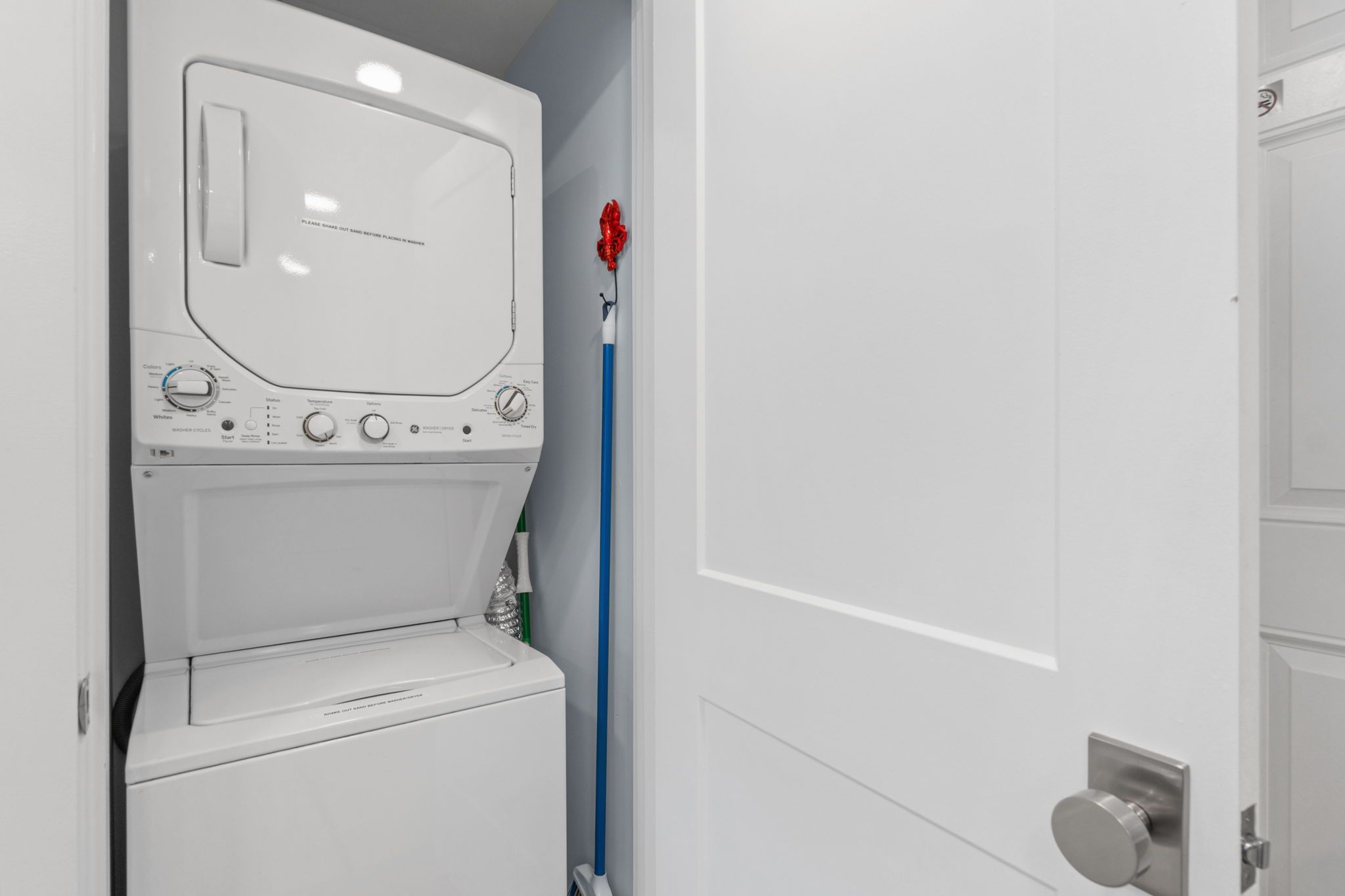 A compact, white laundry room with a front-loading washing machine, a drying rack, and a blue mop.