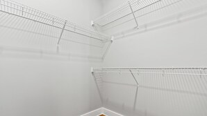A corner closet with metal wire shelving units against a white wall and a wooden floor.