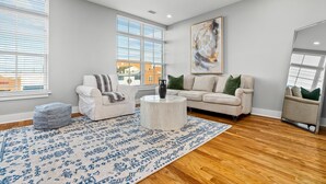 A spacious living room with a large window, a round coffee table, two sofas, and a patterned rug.