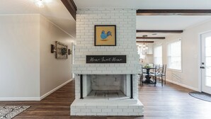 Un salón moderno con chimenea de ladrillo blanco, una obra de arte enmarcada de un gallo, y un cartel que dice 'Home Sweet Home'.
