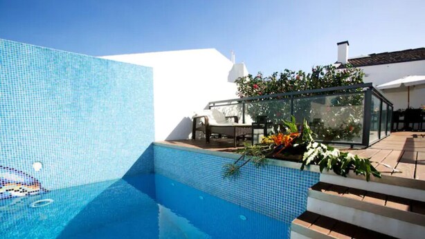 A swimming pool with clear blue water, surrounded by a white wall and a wooden deck. - 2stay - Luxury (Ponta Delgada)