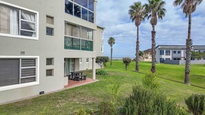 Un edificio moderno a due piani con un balcone, un prato e palme.