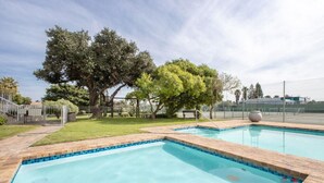 Una piscina rettangolare con bordo piastrellato, circondata da un solarium in mattoni. Si vedono alberi e una recinzione sullo sfondo.
