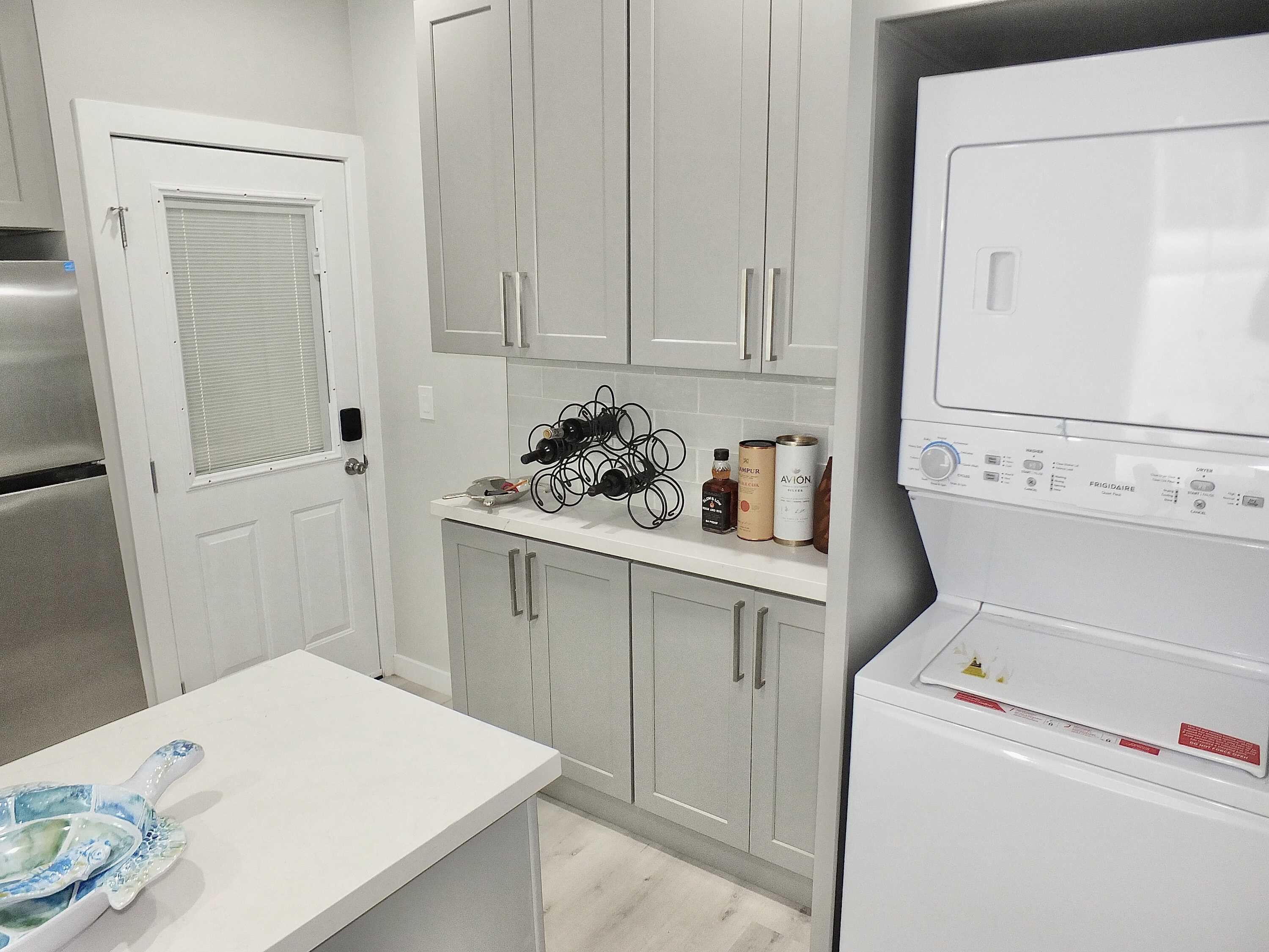 A kitchen with a built-in washer and dryer, a countertop with wine bottles and cans, and a door with a window.