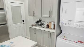 A kitchen with a built-in washer and dryer, a countertop with wine bottles and cans, and a door with a window.